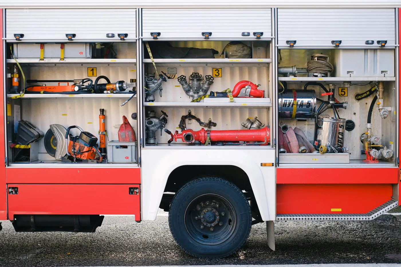 Open equipment bays of a fire engine, stocked with hoses, tools, and rescue gear
